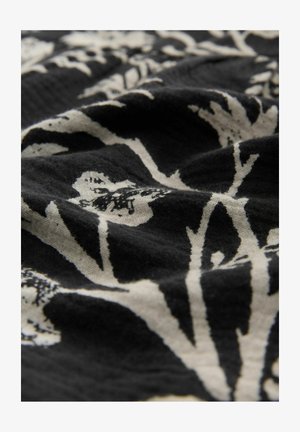 Musta kangas, jossa on kasvitulostus vaaleassa valkoisessa. Suunnittelussa on lehtiä ja oksia, joilla on teksturoitu ulkonäkö.