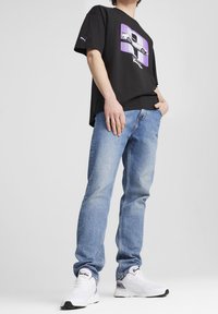 Camiseta de algodón negra con un diseño gráfico que presenta un coche en tonos morados, combinada con jeans de mezclilla azul claro y zapatillas deportivas blancas.