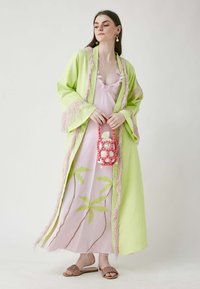 Svijetlozeleni kimono s ružičastim resicama, nošen preko svijetloružičaste haljine s izvezenim zelenim palmama. Model drži ružičastu bisernu torbicu.