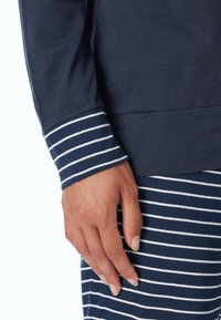 Marinblus med lång ärm och randig manschett. Mjuk material, avslappnad passform, detaljerad med vita ränder på ärmen och skjortan för kontrast.