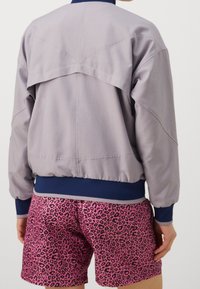Light gray bomber jacket with navy cuffs and collar, featuring a unique back design. Paired with pink leopard print shorts.