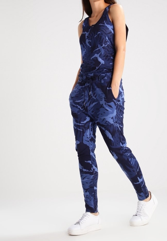 Completo da allenamento blu navy a motivo, composto da una maglietta senza maniche e pantaloni jogging affusolati, realizzato in un materiale morbido ed elasticizzato, abbinato a sneakers bianche.