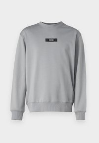 Grå sweatshirt i mjukt tyg, med rund halsringning, ribbade manschetter och en liten svart logotyp på framsidan.