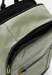 Zaino verde chiaro con parte superiore nera, con esterno testurizzato, doppie cerniere e una tasca interna in rete.