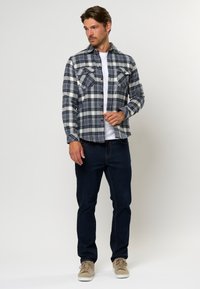 Mėlynos, juodos ir baltos spalvų languota marškiniai su mygtukų užsegimu, dviem krūtinės kišenėmis ir ilgomis rankovėmis, derinami su tamsiomis džinsinėmis kelnėmis ir smėliniais sportbačiais.