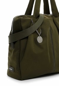 Olive green fabric tote bag with dual handles, zip closure, exterior pocket, and metal tag. Features padded texture and nylon material.
