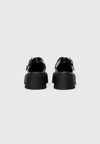 Black platform sandals with rounded toe, adjustable buckle, and textured rubber sole; leather upper with smooth finish.