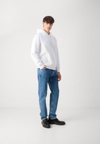 Weißer Baumwoll-Hoodie mit Kordelzug, getragen mit hellblauen geraden Jeans. Schwarze Schuhe vervollständigen das legere Outfit.