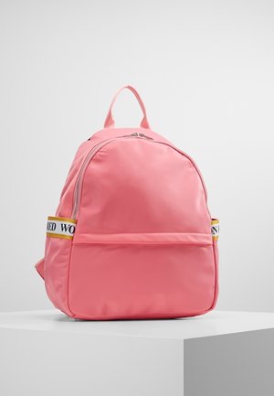Sac à dos rose avec poche zippée à l'avant et bretelles latérales avec accents jaunes, présenté sur un socle blanc devant un fond gris uni.