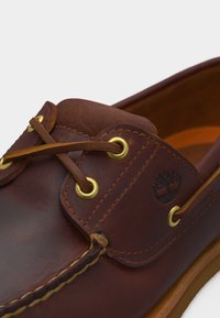 Bruine leren bootsschoen met leren veters door gouden oogjes geregen en een boomlogo op het zijpaneel gegraveerd.