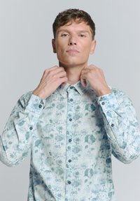 Lichtblauwe overhemden met een bloemenprint in donkerdere tinten. Heeft een puntige kraag en lange mouwen met knoopmanchetten.