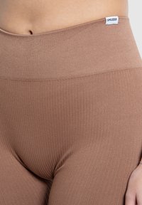 Leggings marroni a costine con una cintura larga ed elastica. Il tessuto sembra morbido ed elastico, con un piccolo logo etichetta sulla cintura.