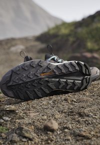 Czarne buty trekkingowe z podeszwami marki Continental odpoczywające na skalistym terenie na zewnątrz.