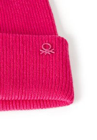 Růžová pletená čepice s žebrovaným vzorem, s ohrnutým lemem a malým kruhovým logem vpředu.