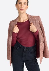 Haut à manches longues burgundy à côtes, associé à un blazer texturé en pied-de-poule marron et à un jean noir taille haute.