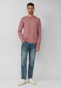 Rot gepunkteter Strickpullover mit Rundhalsausschnitt, kombiniert mit hellblauen Jeans und weißen Sneakers. Der Pullover hat lange Ärmel und gerippte Bündchen.