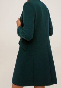 Cappotto in misto lana color teal con design strutturato, colletto e maniche lunghe. Silhouette a forma di A, texture liscia e tasche laterali invisibili.