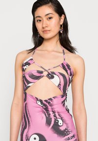 Vestido rosa com padrões abstratos em preto e branco, apresentando um design recortado e alças finas. Tecido liso e elástico. Acentuado com um anel frontal.