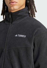 Black fleece zip-up jacket featuring a high collar, smooth texture, and a white "TERREX" logo on the front.