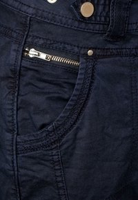Pantalons bleu marine avec un tissu texturé, des coutures visibles, une poche zippée sur le côté avec un matériel métallique, et un design classique de poche.
