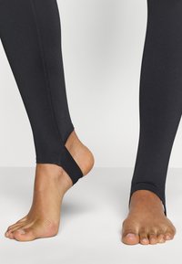 Μαύες κολάν με κόψιμο στους αστραγάλους, εφαρμοστή σχεδίαση, λείο υλικό και ορατές ραφές. Εκτεθειμένα πόδια που δείχνουν τον φυσικό τόνο του δέρματος.