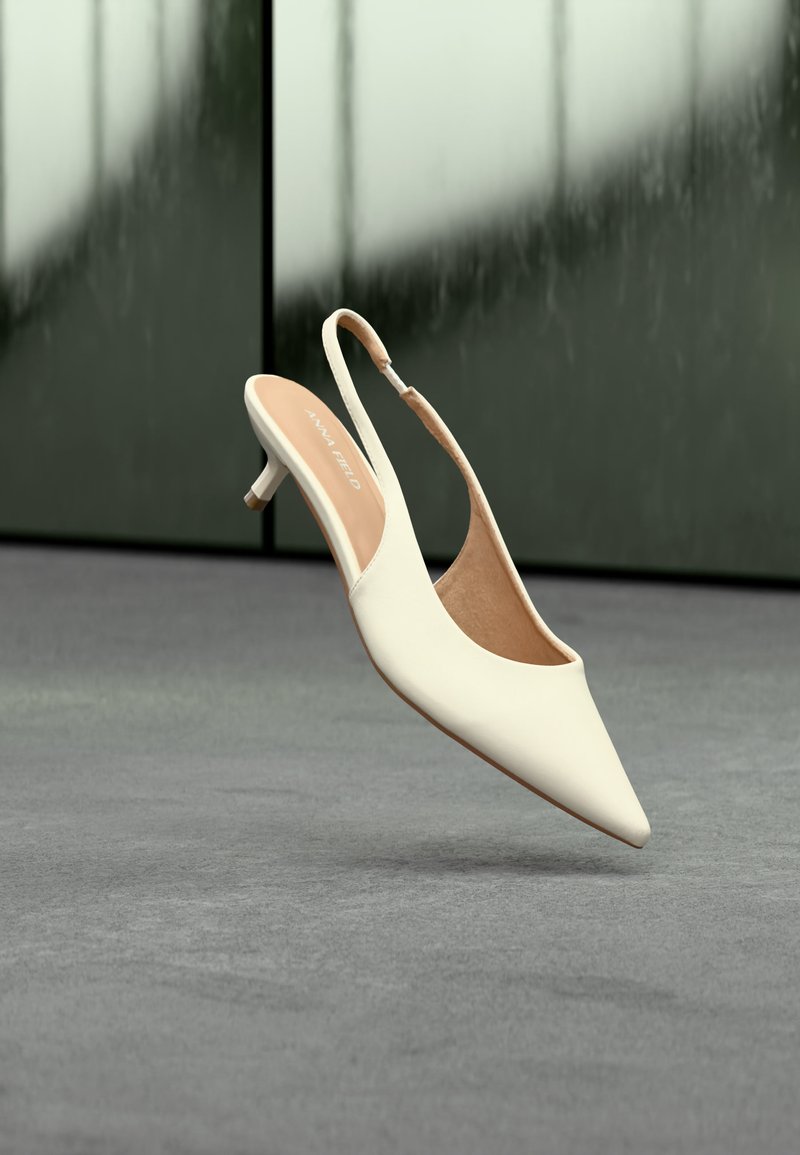 Μπεζ γυναικείο παπούτσι slingback με μυτερό μύτη και χαμηλό τακούνι kitten που αιωρείται πάνω από γκρι πάτωμα με θολό σκοτεινό φόντο.