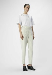 Camiseta blanca con acentos bordados circulares, combinada con pantalones ajustados de color claro y mules de cuña negra, con una textura suave.