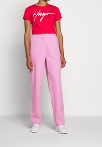 Camisa de algodón roja con texto blanco "Hugo", combinada con pantalones de talle alto rosa y zapatillas blancas, con un corte recto.