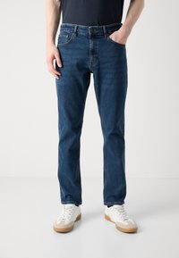 Jeans bleumarin din denim, cu un croi drept, cinci buzunare, cusături contrastante și închidere cu buton, asortați cu teniși albi.