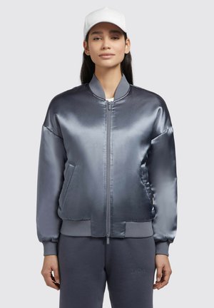 Grå satin bomberjacka med ribbad mudd. Har en dragkedja framtill, sidofickor och en slät, glänsande yta. Bärs med matchande grå sweatpants.