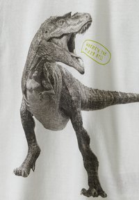 Balta marškinėliai su detaliu juodos ir pilkos spalvos piešiniu, vaizduojančiu dinozaurą su kalbos burbulu, kuris sako "KUR PICA??"