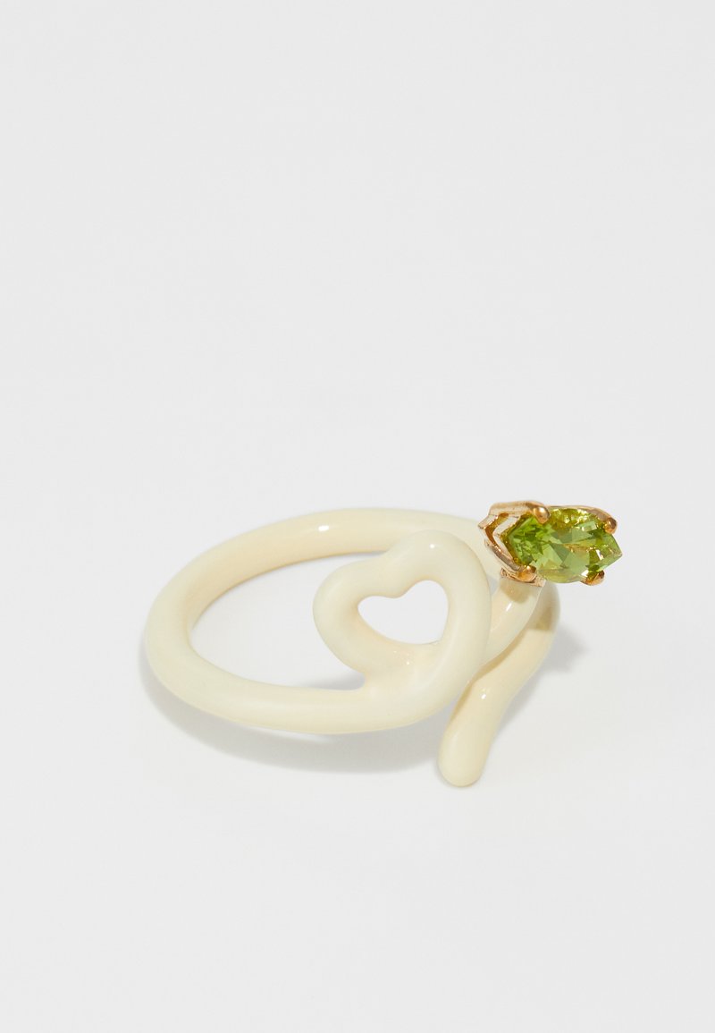 Inel din ceramică albă cu un design răsucit, având o formă de inimă și un montaj din aur pentru un accent de piatră verde.