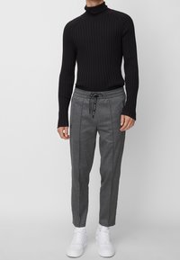 Svart ribbad polotröja i kombination med grå tapered-byxor med dragsko och sidofickor, kompletterat med vita sneakers.