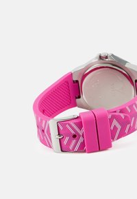 Rosa silikonarmband med en texturerad mönstring och silverfärgad hardware, med ett spänne och en slät undersida.