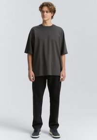Tricou oversized de culoare gri închis, cu guler rotund, mâneci scurte și croială dreaptă, asortat cu pantaloni negri și pantofi bleumarin.