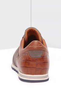 Brązowy skórzany sneaker z teksturowanym akcentem w kształcie krokodyla na pięcie, szara zamszowa cholewka, okrągły nos i kontrastowa biała podeszwa.