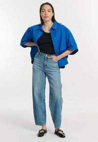 Niebieska, oversize'owa koszula z guzikami z przodu, czarny dopasowany top na ramiączkach, jasnoniebieskie jeansy z wysokim stanem oraz czarne baleriny.