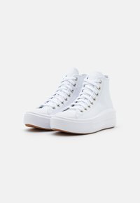 Białe trampki za kostkę wykonane z gładkiego płótna, z metalowymi oczkami, okrągłym noskiem oraz grubą białą gumową podeszwą o fakturowanej powierzchni.