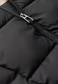 Sezione di giacca a vento nera con zip, texture liscia, design trapuntato e materiale lucido con dettagli in metallo argentato.