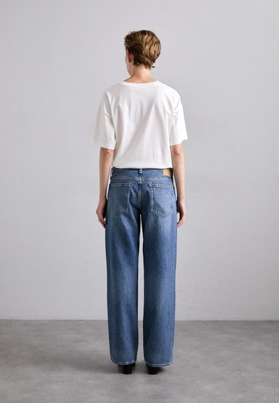 White cotton t-shirt with short sleeves, paired with high-waisted, wide-leg blue denim jeans. Features two back pockets and a seamless design.