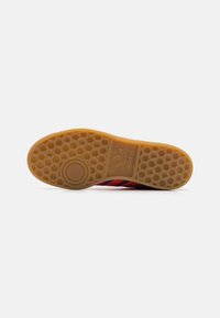 Adidas sneakersula i tan gummi med hexagonala mönster och cirkulära accenter. Har röda och marinblå ränder på en texturerad yta.