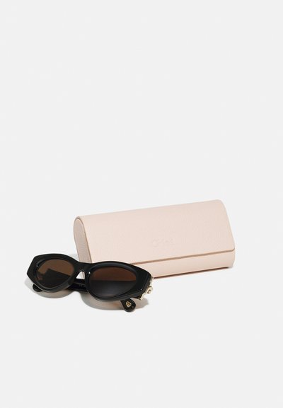 Schwarze Sonnenbrille mit einem markanten, kantigen Design und dunklen Gläsern, nebeneinem hellrosa Lederetui mit strukturiertem Finish und eingeprägtem Logo.