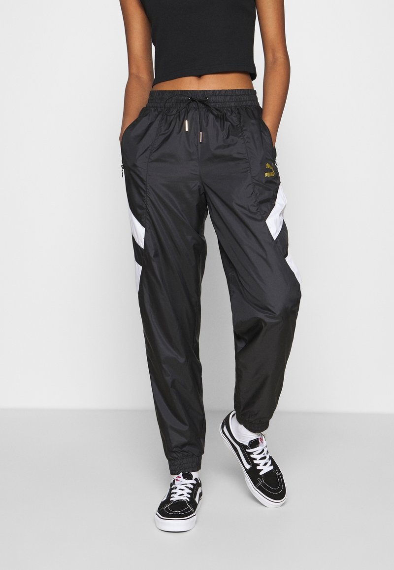 Svarta vindjacka byxor med vita detaljer, elastiska muddar och dragsnöre i midjan. Har dragkedjefickor och branding. Slät yta.