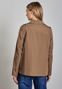 Giacca leggera marrone con design a colletto, caratterizzata da una vestibilità dritta, dettagli con bottoni sulle spalle e una texture liscia.