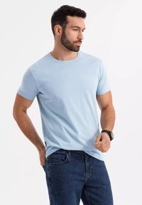 Světle modré bavlněné tričko s kulatým výstřihem, krátkými rukávy a uvolněným střihem, v kombinaci s tmavě modrými džíny a černými hodinkami.