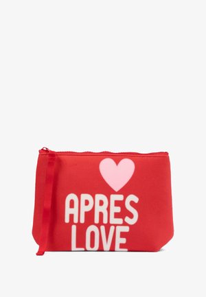 Czerwona saszetka z białym napisem "APRES LOVE", z różowym sercem, wykonana z miękkiego materiału, z zamknięciem na zamek błyskawiczny i wstążkowym uchwytem.
