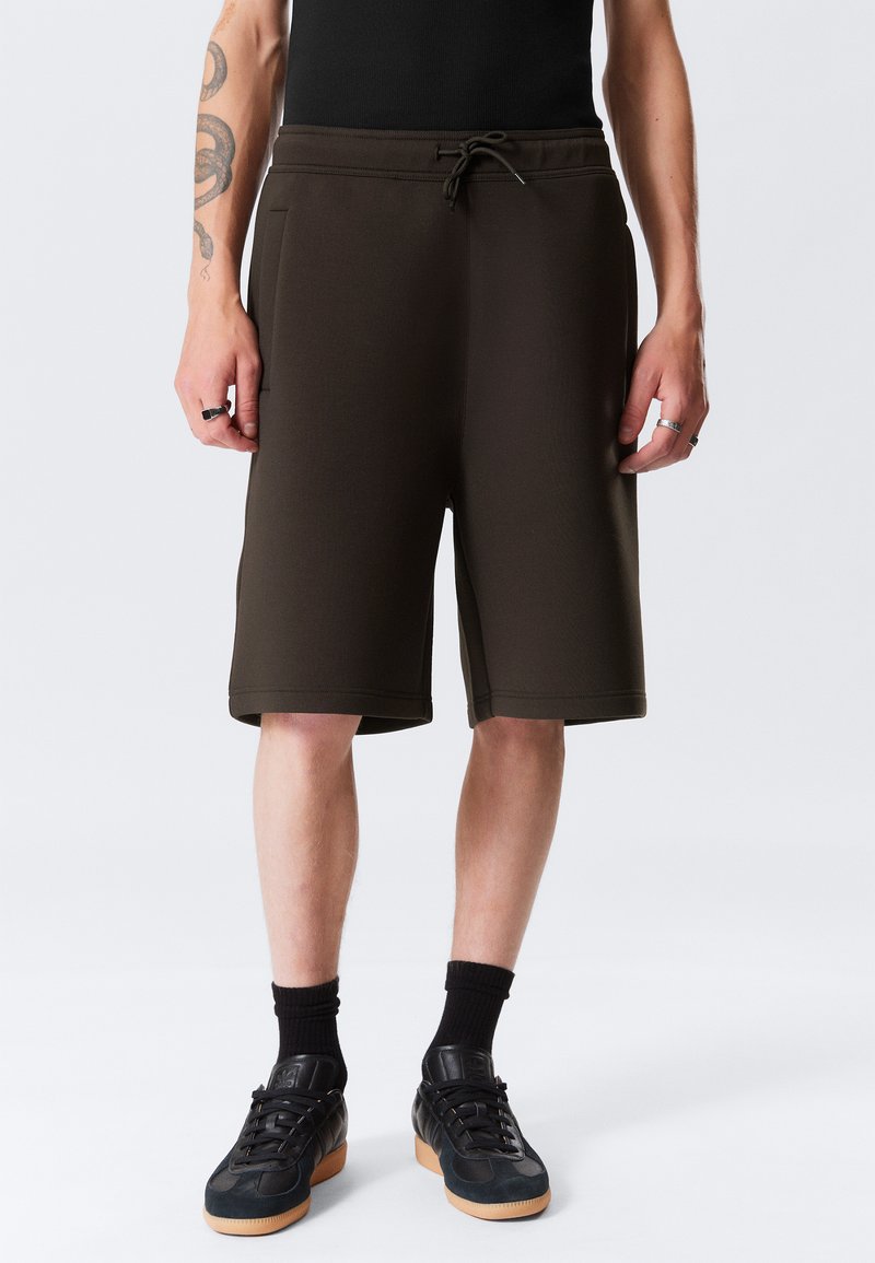 Pantaloni sportivi marroni con una vestibilità rilassata, realizzati in materiale morbido, dotati di un elastico in vita, cordoncino e tasche laterali.