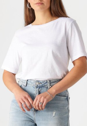 Biele tričko s krátkym rukávom vyrobené z jemnej látky, s voľným strihom. Spárované so svetlomodrými vysokými džínsami s opotrebovaním.