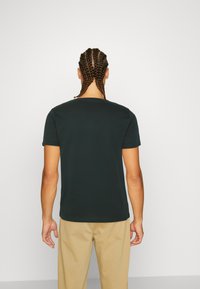 Cămașă scurtă de culoare verde închis, cu gât rotund, design simplu, confecționată din bumbac, văzută din spate. Textură netedă, fără modele vizibile.