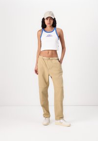Hvid crop top med blå kant, der har et logo; beige løse bukser med lommer og bælte; lyse sneakers; neutral baggrund.